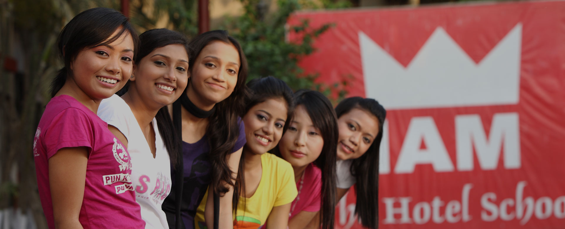 Group of smiling students at IAM, the best hotel management institute in India, standing in front of the campus banner.