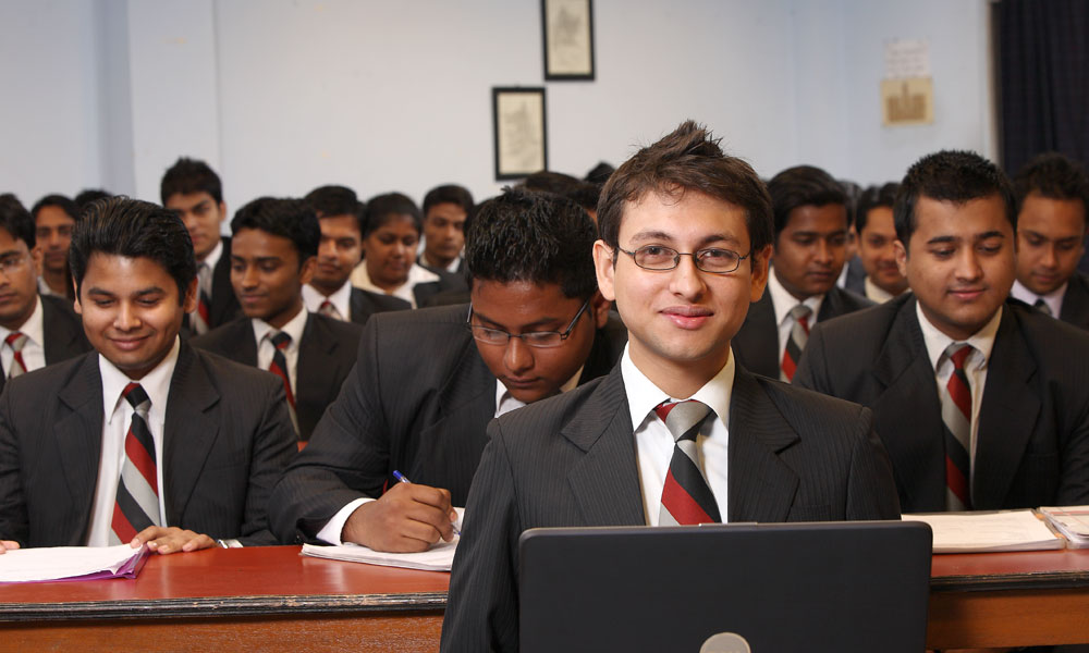 Students pursuing bachelor degree in hotel management attending a classroom session in formal uniforms, focused and engaged.