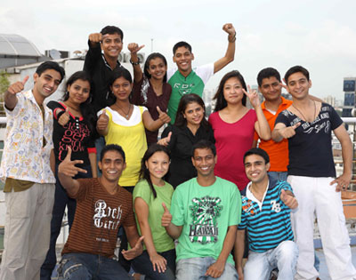 Group of students pursuing bachelor degree in hotel management enjoying campus life, posing cheerfully on a sunny rooftop setting.