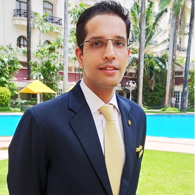 Our Industry Expert Mayan Dhawan, from the best hotel management institute, in a navy suit by the poolside of a luxury hotel.